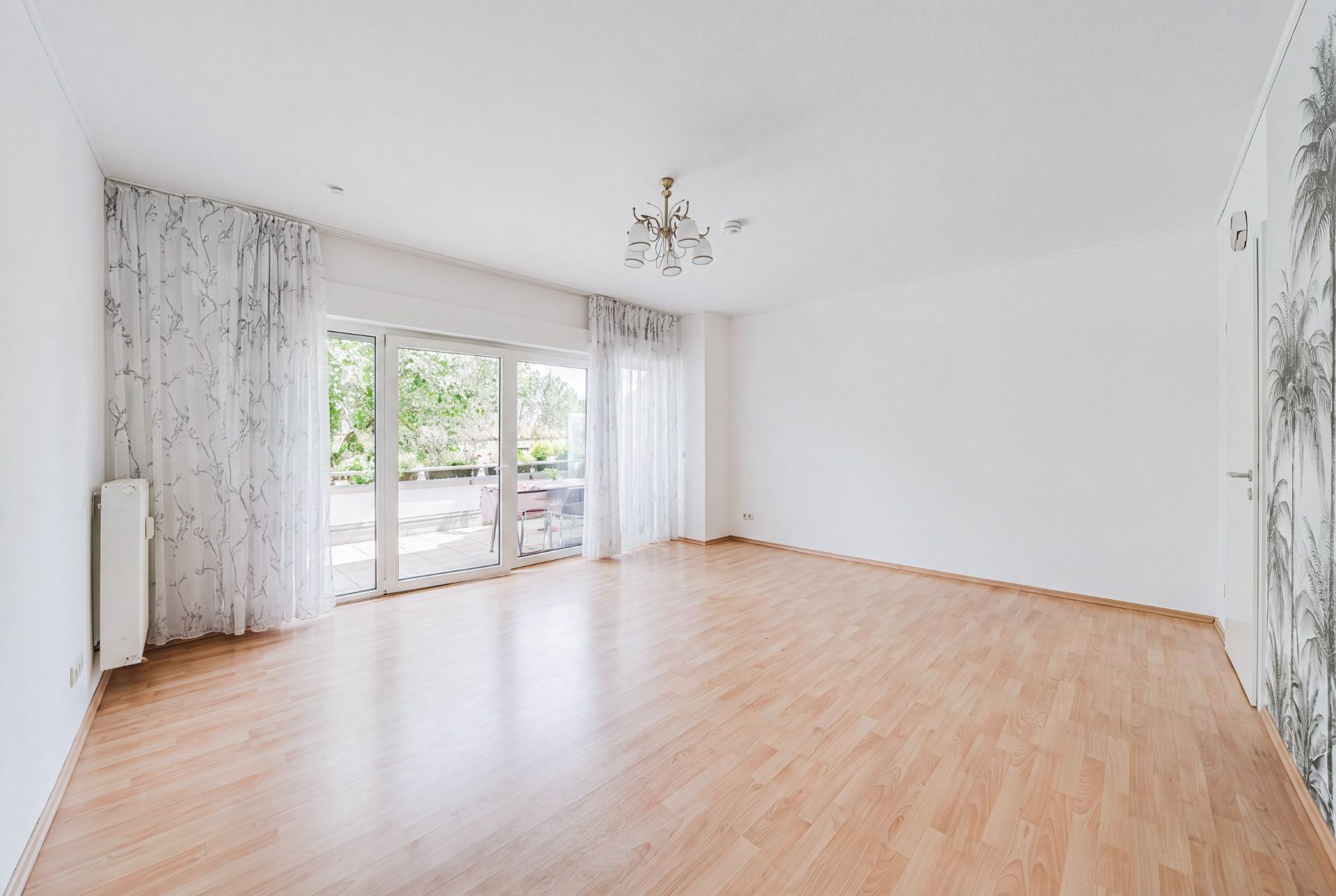 Heller, leerer Raum mit Holzfußboden, großen Fenstern und Vorhängen.