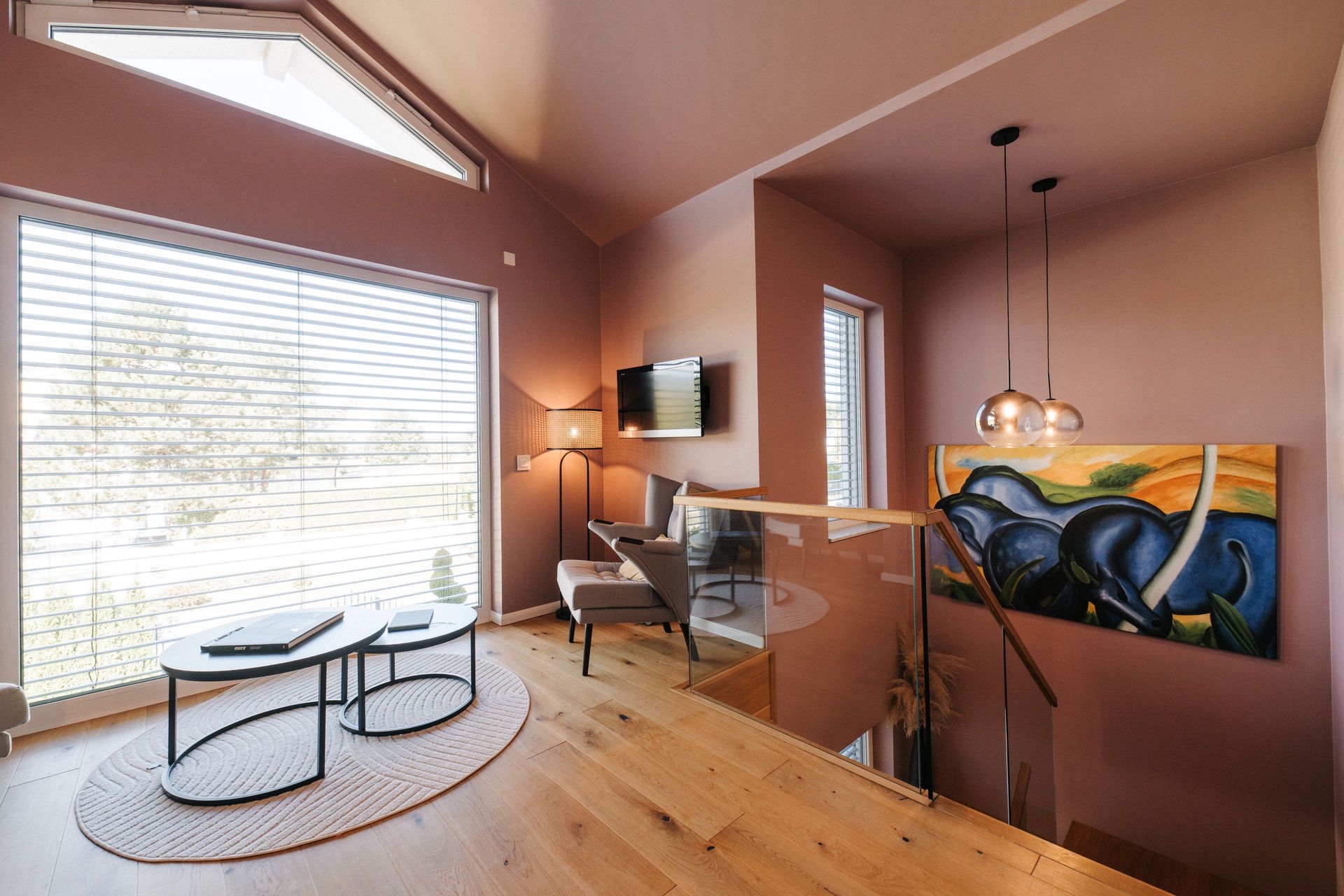 Modernes Wohnzimmer mit großen Fenstern, Sesseln, Couchtischen und farbigem Gemälde an der Wand.