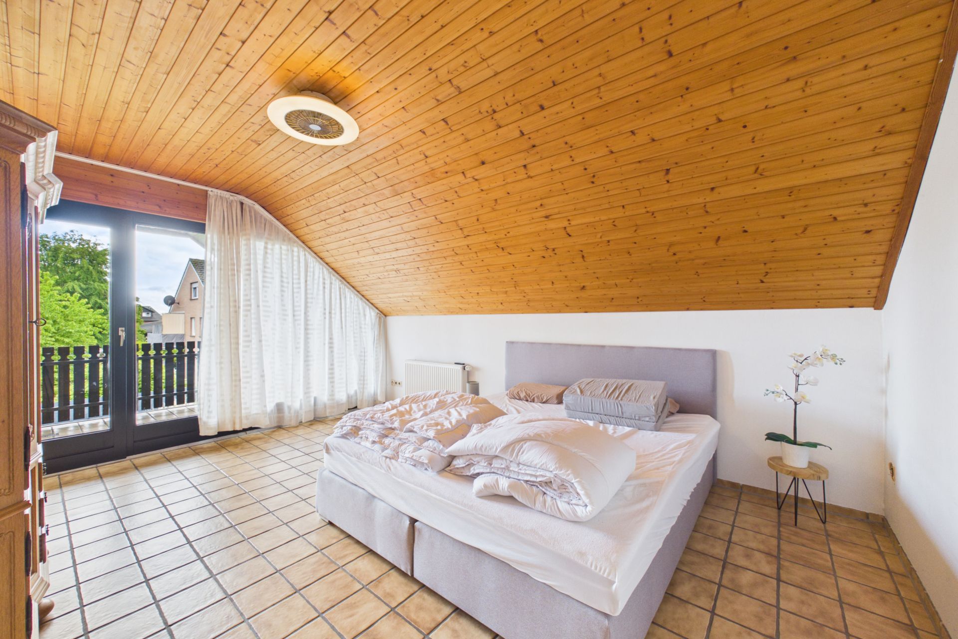 Helles Schlafzimmer mit Doppelbett, Schräge, Fliesenboden und Balkonzugang.