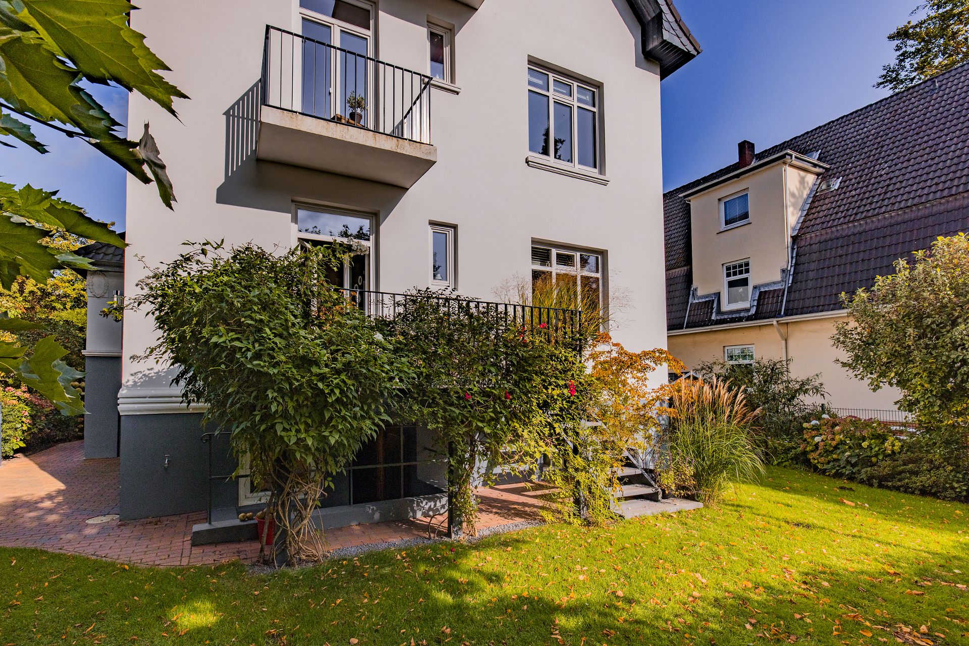 Wohnhaus mit Balkon, Terrasse und grünem Garten, umgeben von Büschen und Pflanzen.