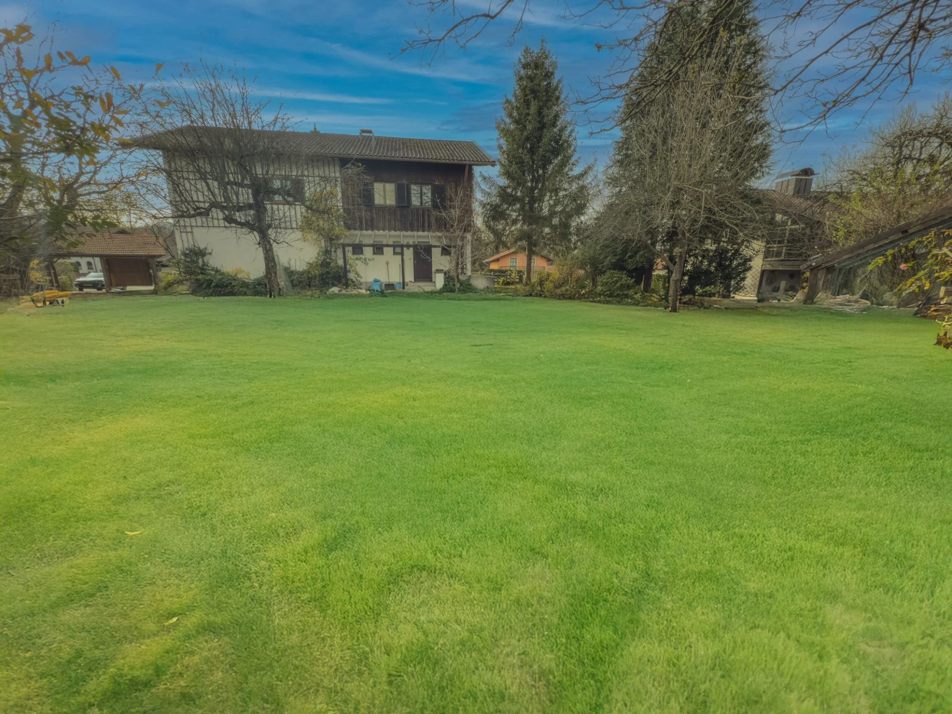 Großer grüner Garten mit Bäumen und einem zweistöckigen Wohnhaus im Hintergrund.
