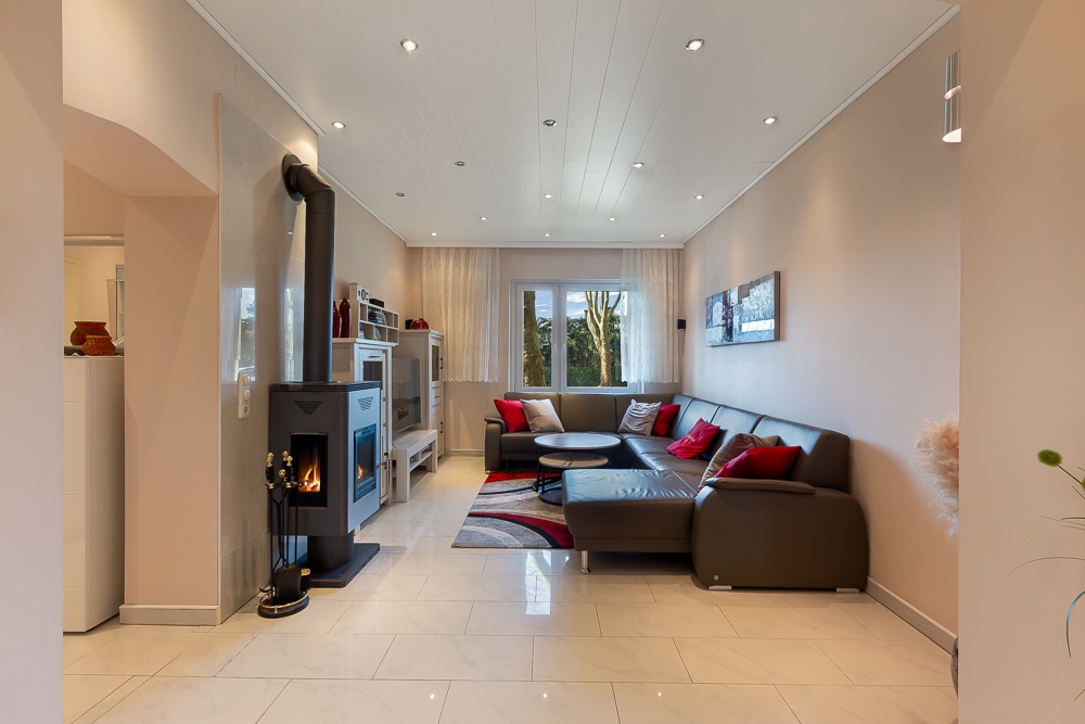 Wohnzimmer mit Kaminofen, braunem Ecksofa, Couchtisch und großem Fenster.