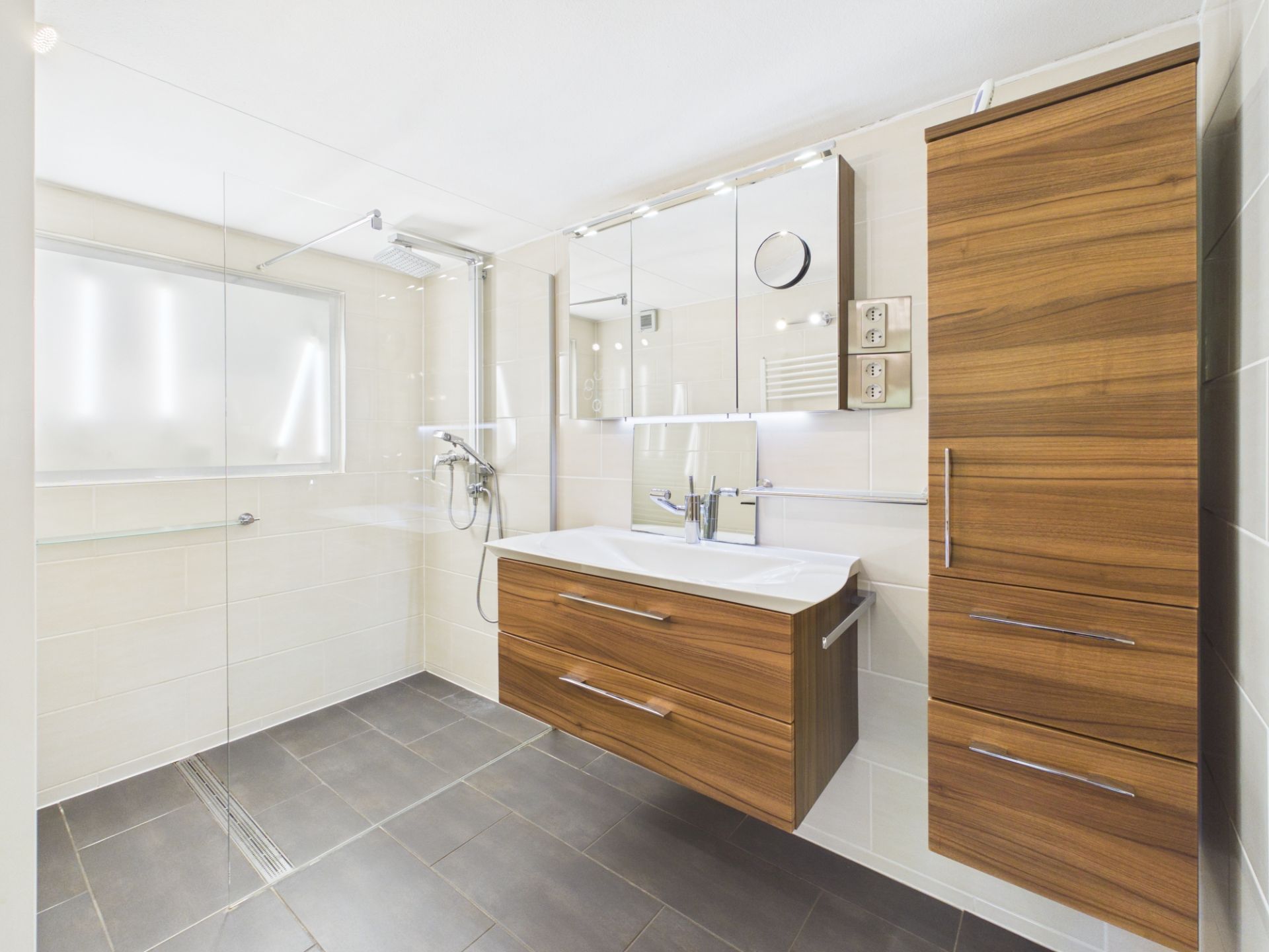 Modernes Badezimmer mit Holzmöbeln, Waschtisch, Spiegel und ebenerdiger Dusche.