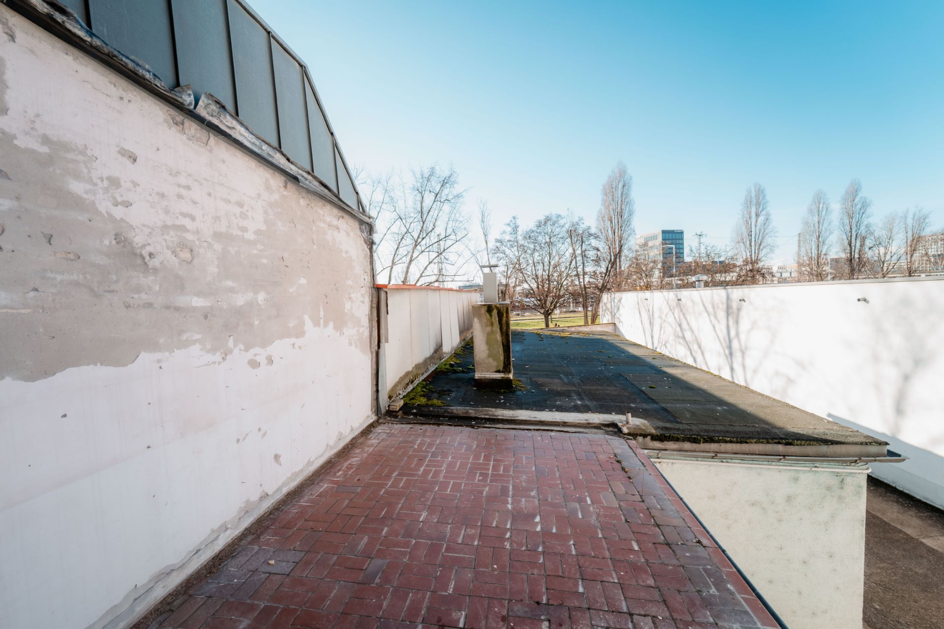 Ziegelterrasse mit angrenzender Flachdachfläche und Blick auf Bäume im Freien.