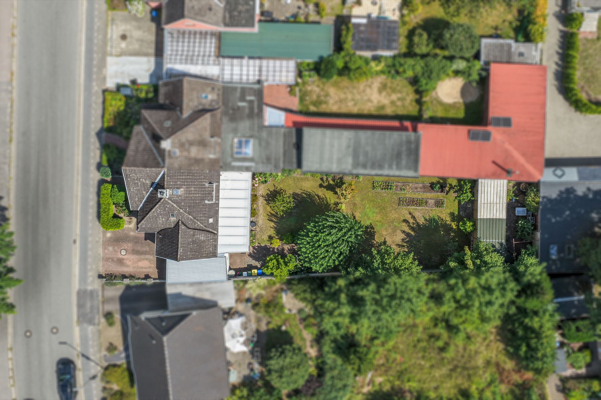 Luftaufnahme eines Wohnhauses mit Garten, Nebengebäuden und angrenzender Straße.