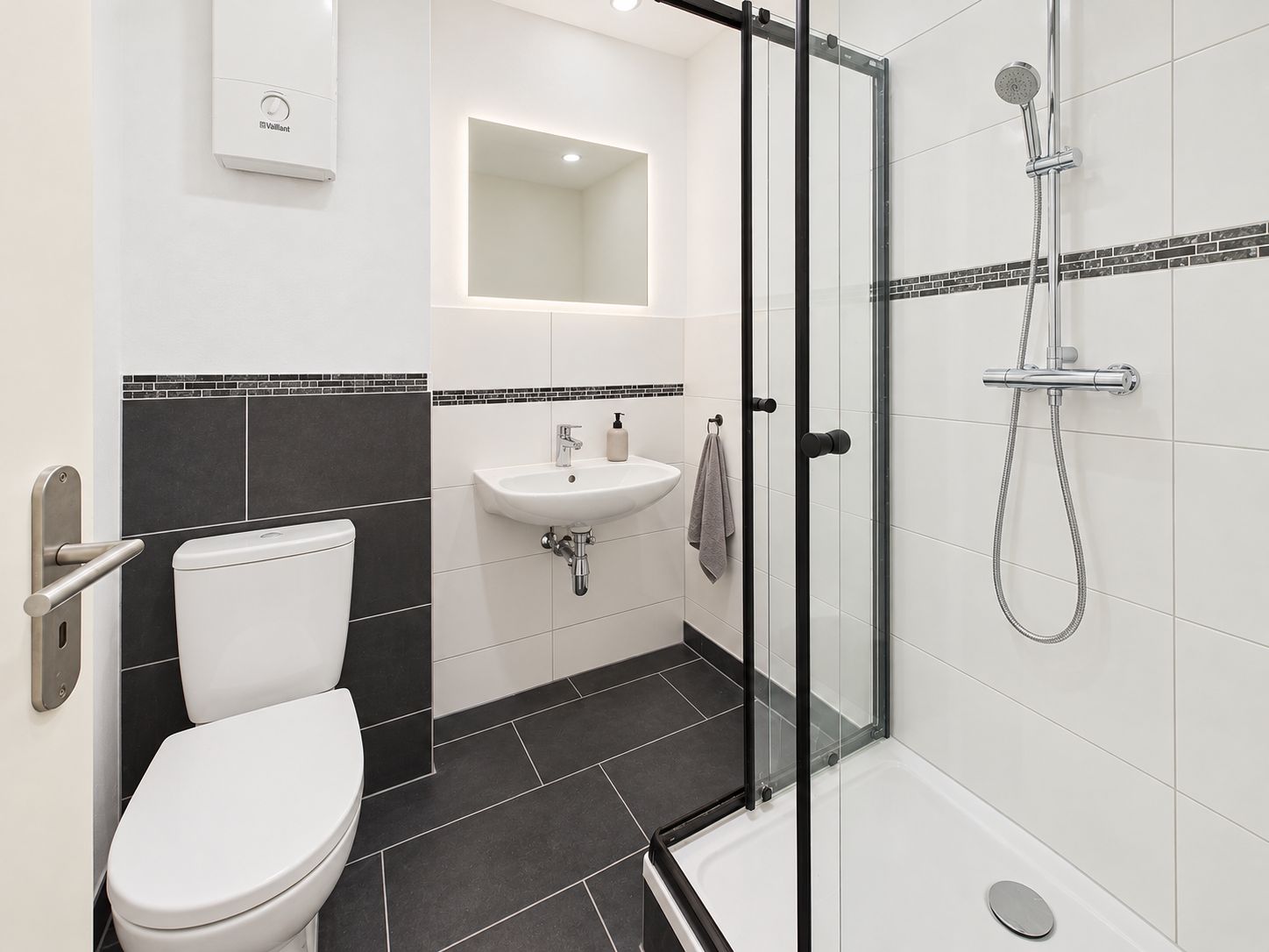 Modernes Badezimmer mit Dusche, Toilette, Waschbecken und beleuchtetem Spiegel.
