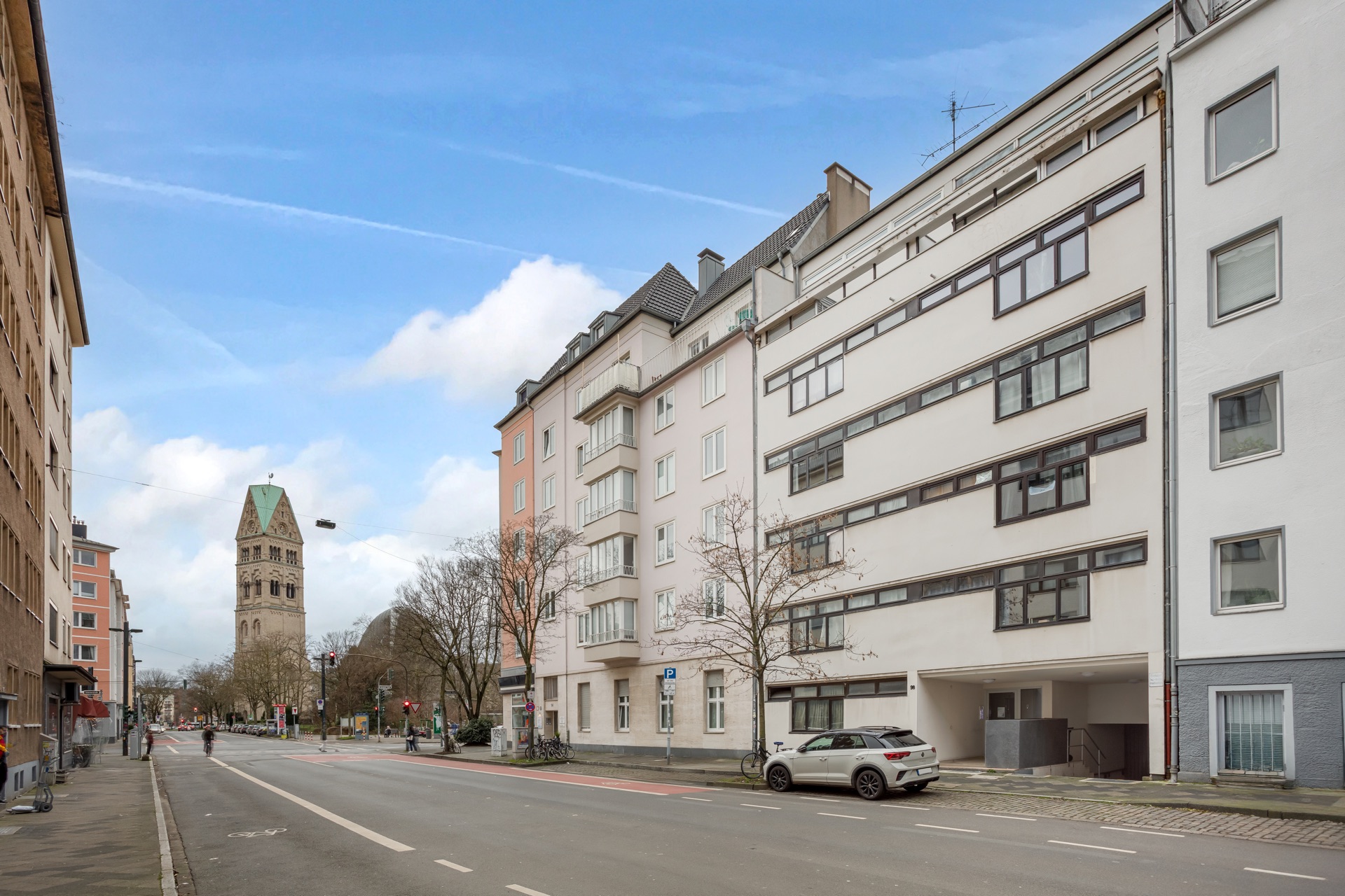 Wohngebäude an einer ruhigen Straße mit geparktem Auto und Kirchturm im Hintergrund.