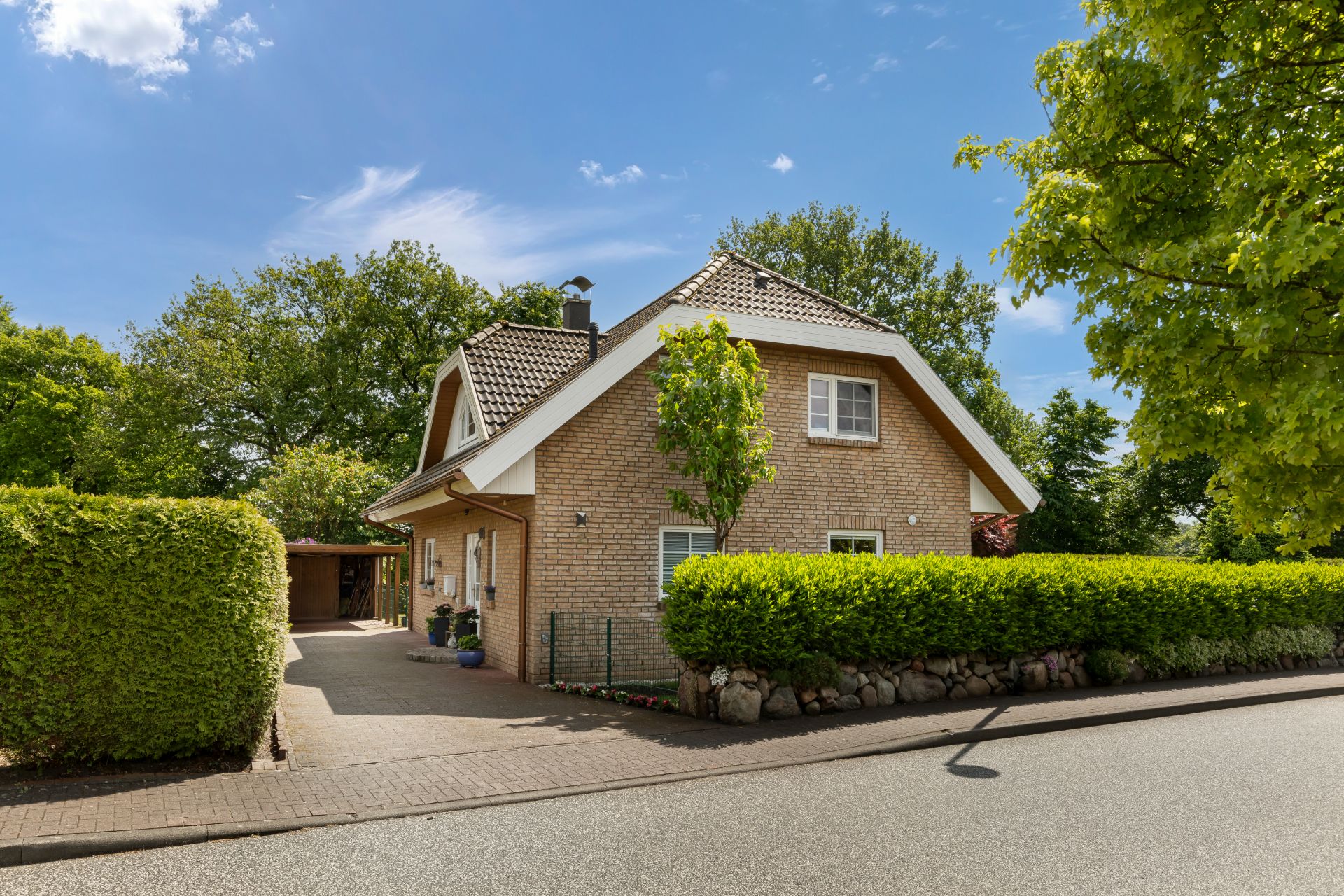 Einfamilienhaus mit Satteldach, Garten und Einfahrt, umgeben von Bäumen und Hecken.