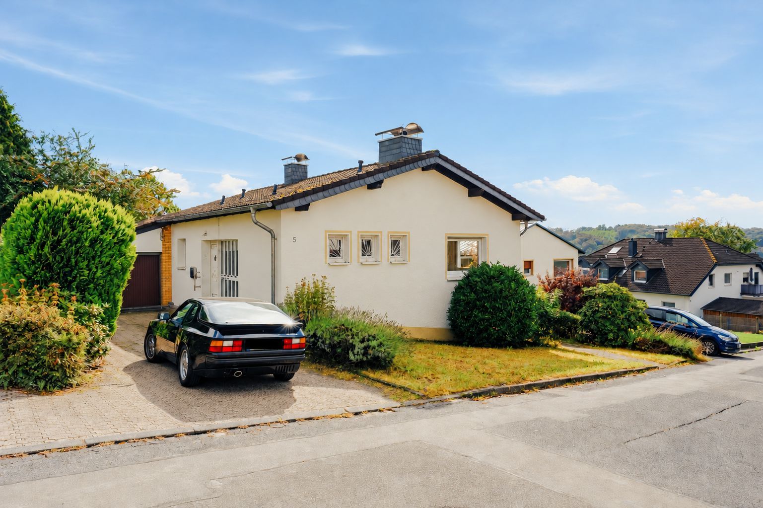 Einfamilienhaus mit hellem Putz, Vorgarten, gepflasterter Einfahrt und geparktem Auto.
