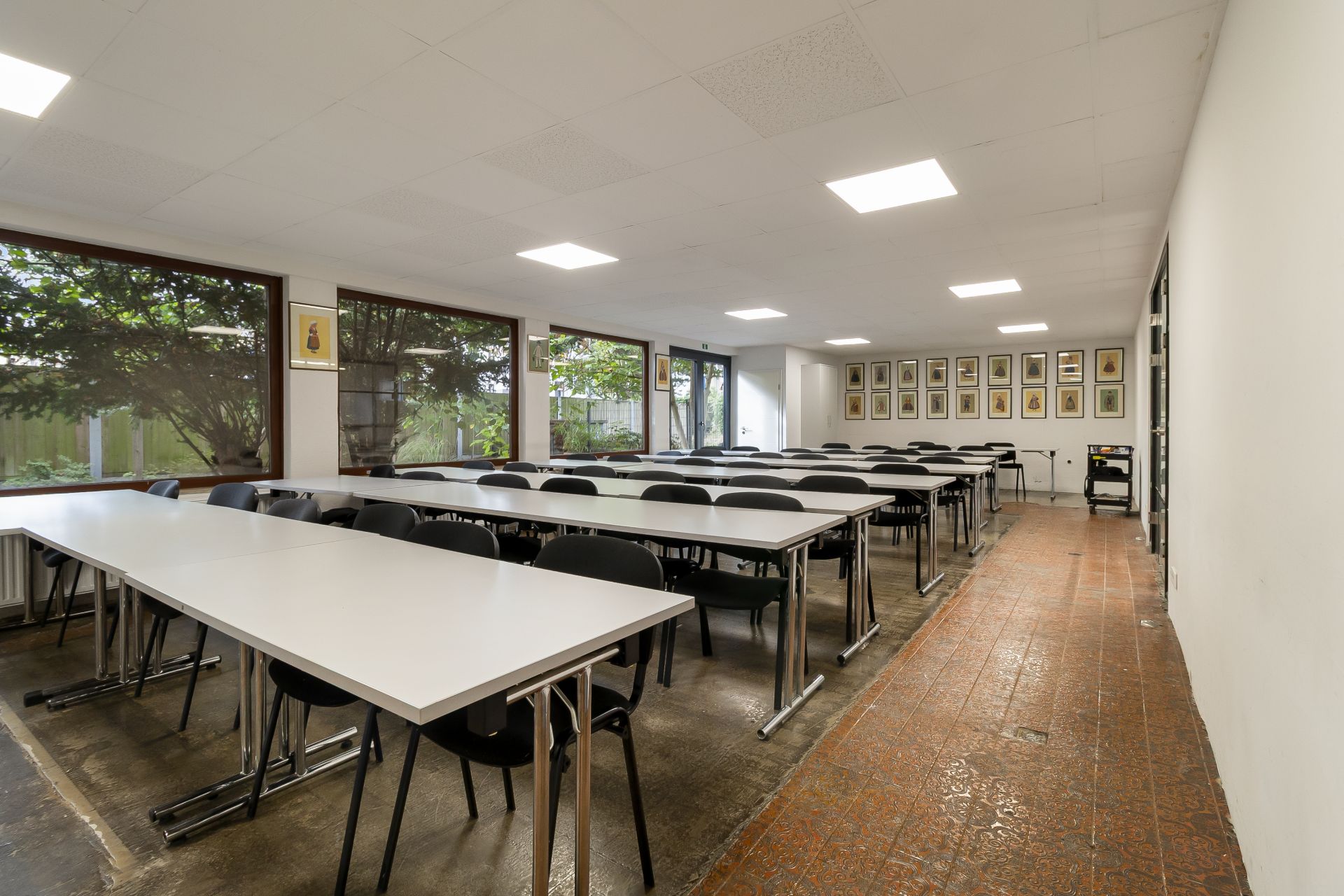 Heller Raum mit langen Tischen und vielen Stühlen, große Fenster an der Seite.