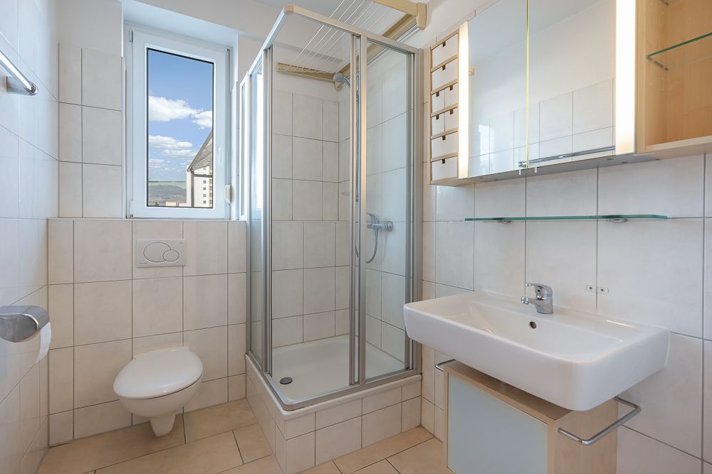 Helles, modernes Badezimmer mit Dusche, WC, Waschbecken und Fenster.