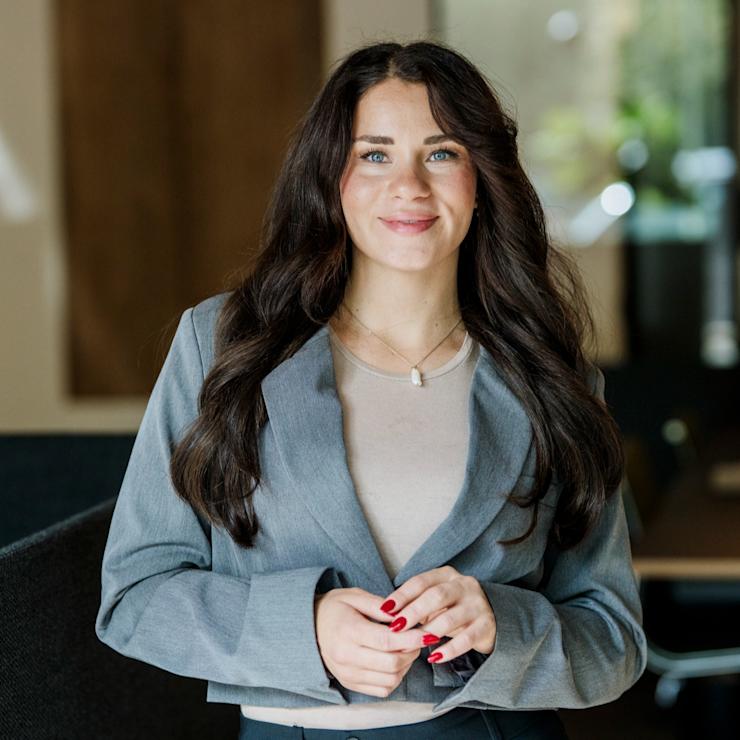 Junge Frau mit langen dunklen Haaren steht in einem modernen Raum.