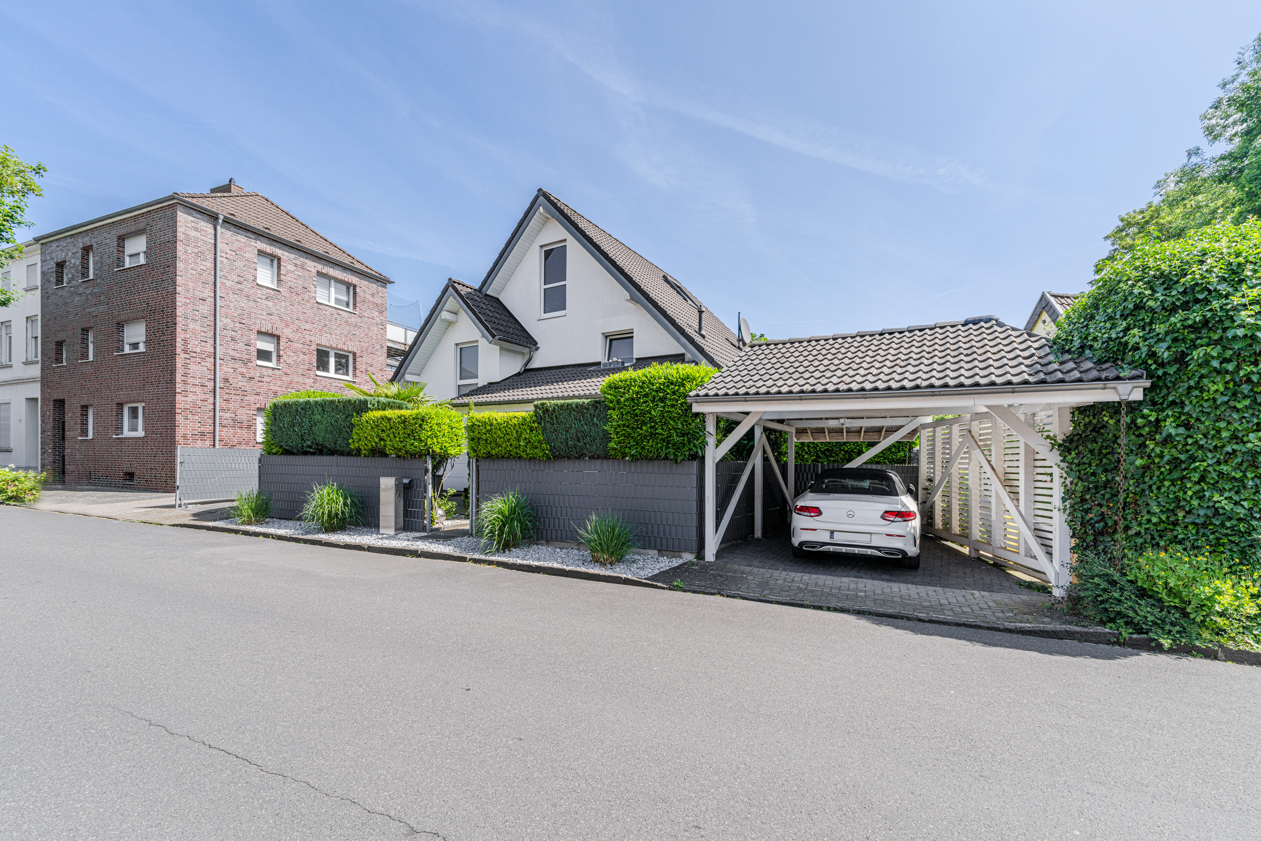 Wohnhaus mit Carport, in dem ein weißes Auto steht, und gepflegtem Vorgarten an einer ruhigen Straße.