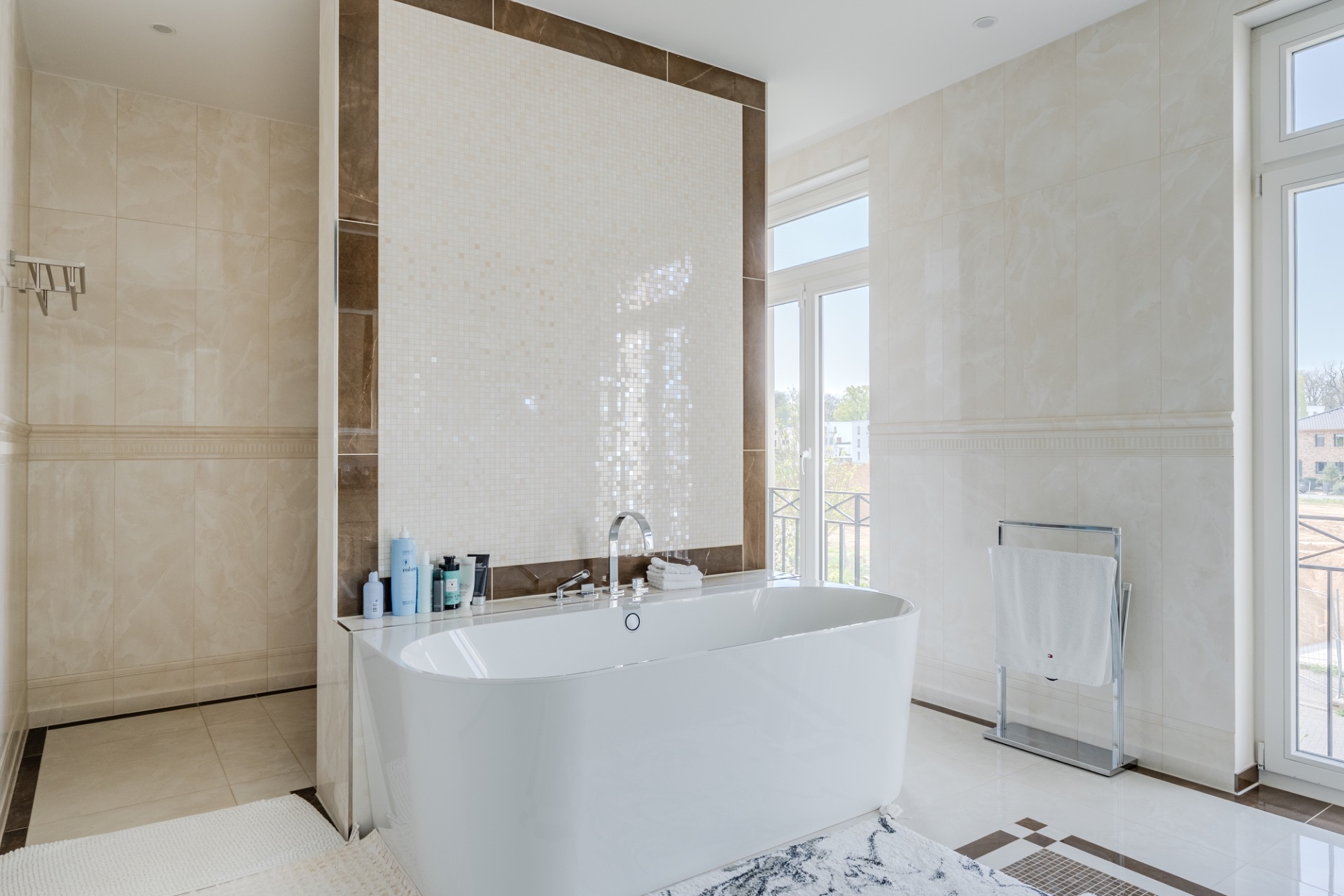 Helles Badezimmer mit freistehender Badewanne, Handtuchständer und großen Fenstern.