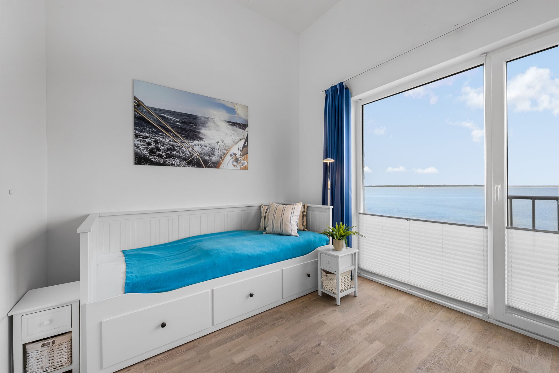 Helles Zimmer mit Einzelbett, Nachttisch und großem Fenster mit Blick auf das Wasser.