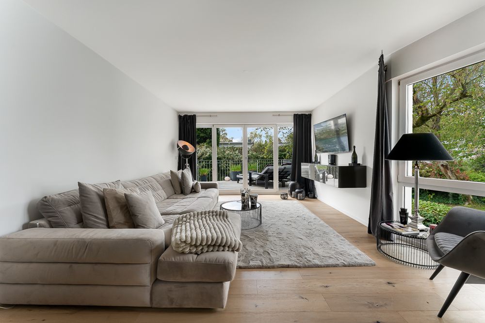 Wohnzimmer mit großem Sofa, Couchtisch, Teppich und bodentiefen Fenstern mit Blick ins Grüne.