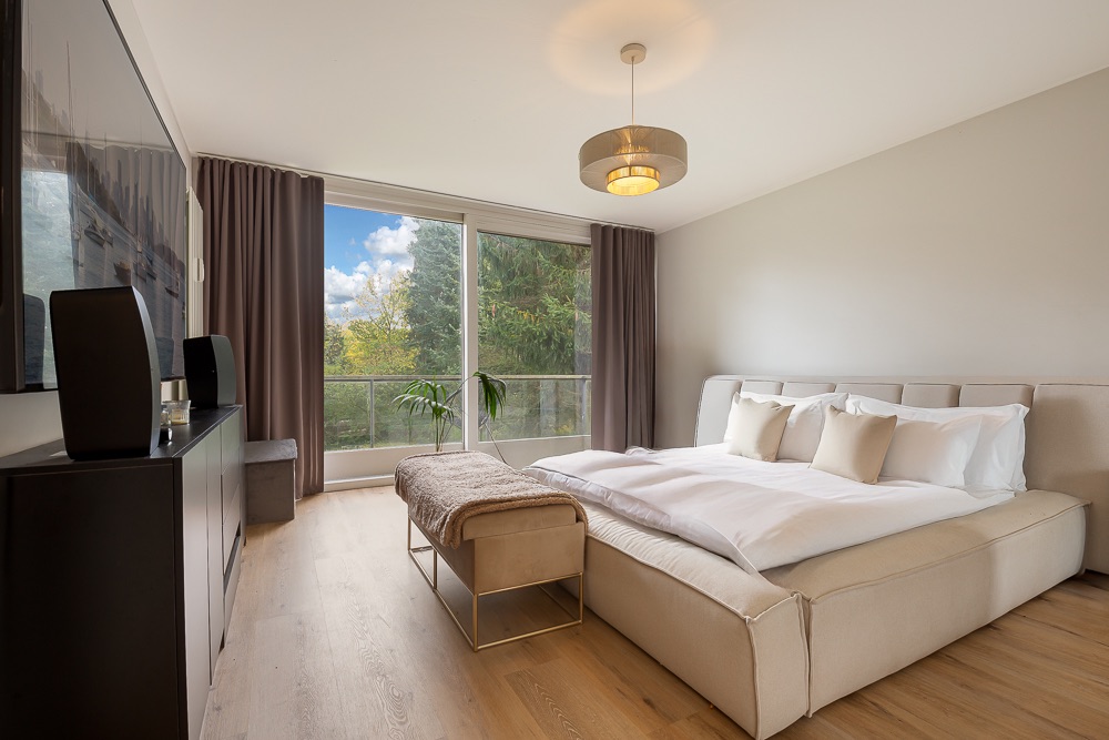Modernes Schlafzimmer mit Doppelbett, großer Fensterfront und Blick ins Grüne.