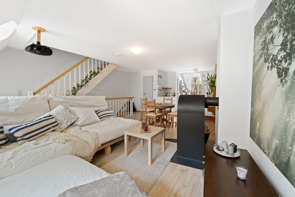 Helles Wohnzimmer mit Sofa, Esstisch, Treppe und Holzofen, moderne Einrichtung.