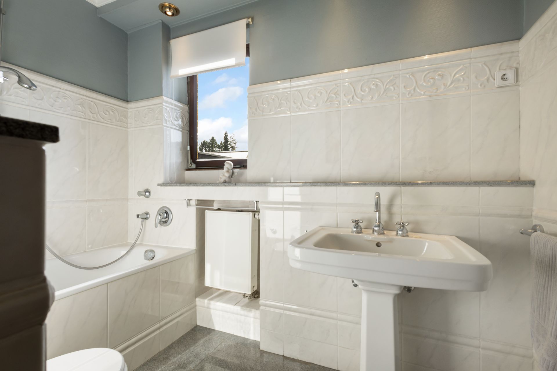 Helles Badezimmer mit Badewanne, Waschbecken, Fenster und weißen Fliesen.