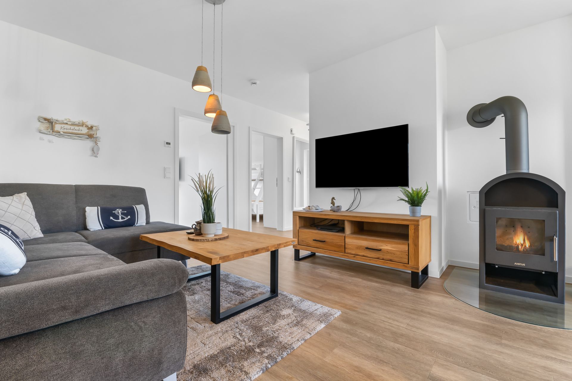 Modernes Wohnzimmer mit grauem Sofa, Holztisch, Kamin, TV und Holzschrank auf Holzboden.