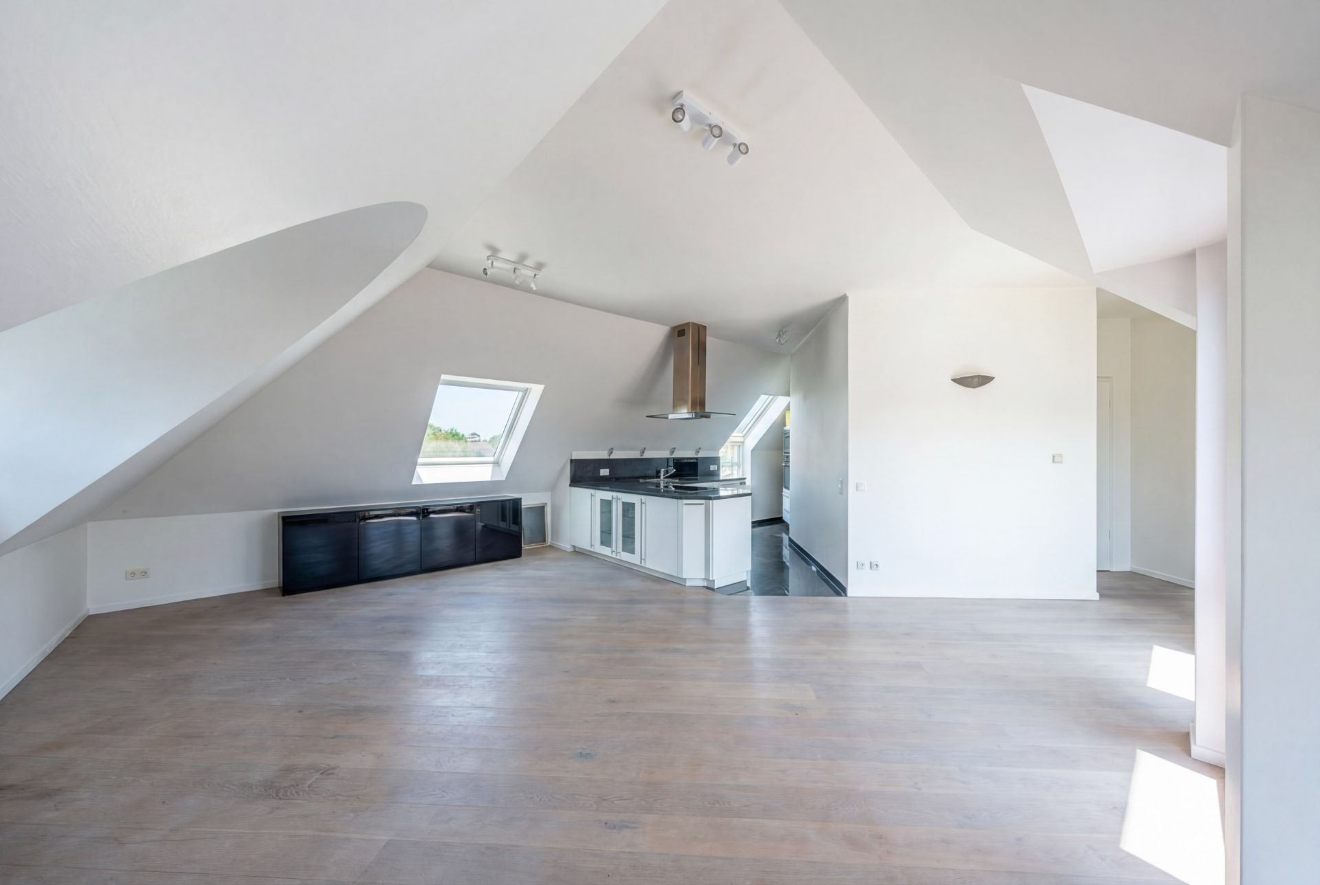 Helles Dachgeschosszimmer mit offener Küche, Holzfußboden und großen Fenstern.