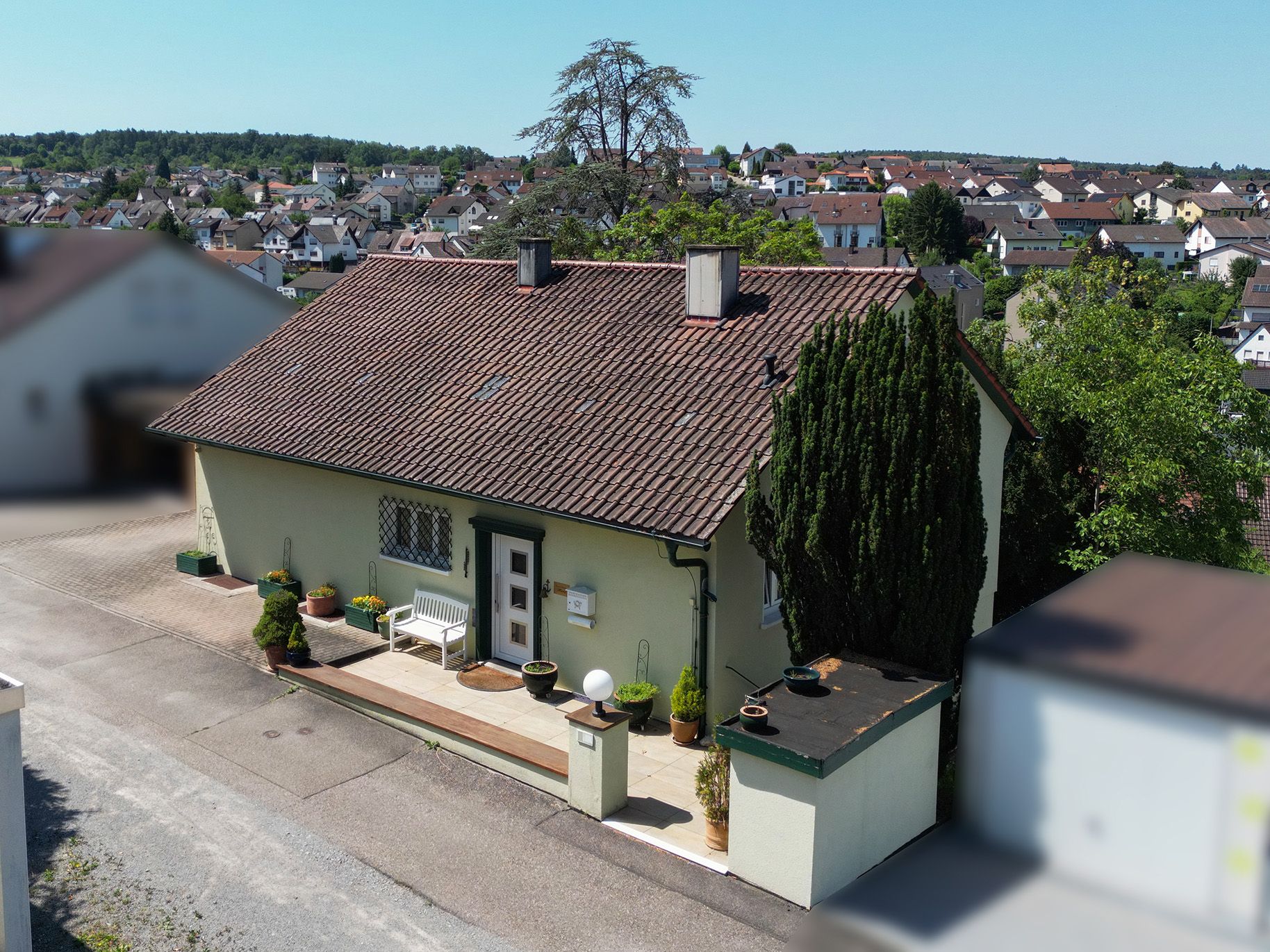 Ein Einfamilienhaus mit Ziegeldach, Vorgarten und Bank vor dem Eingang.