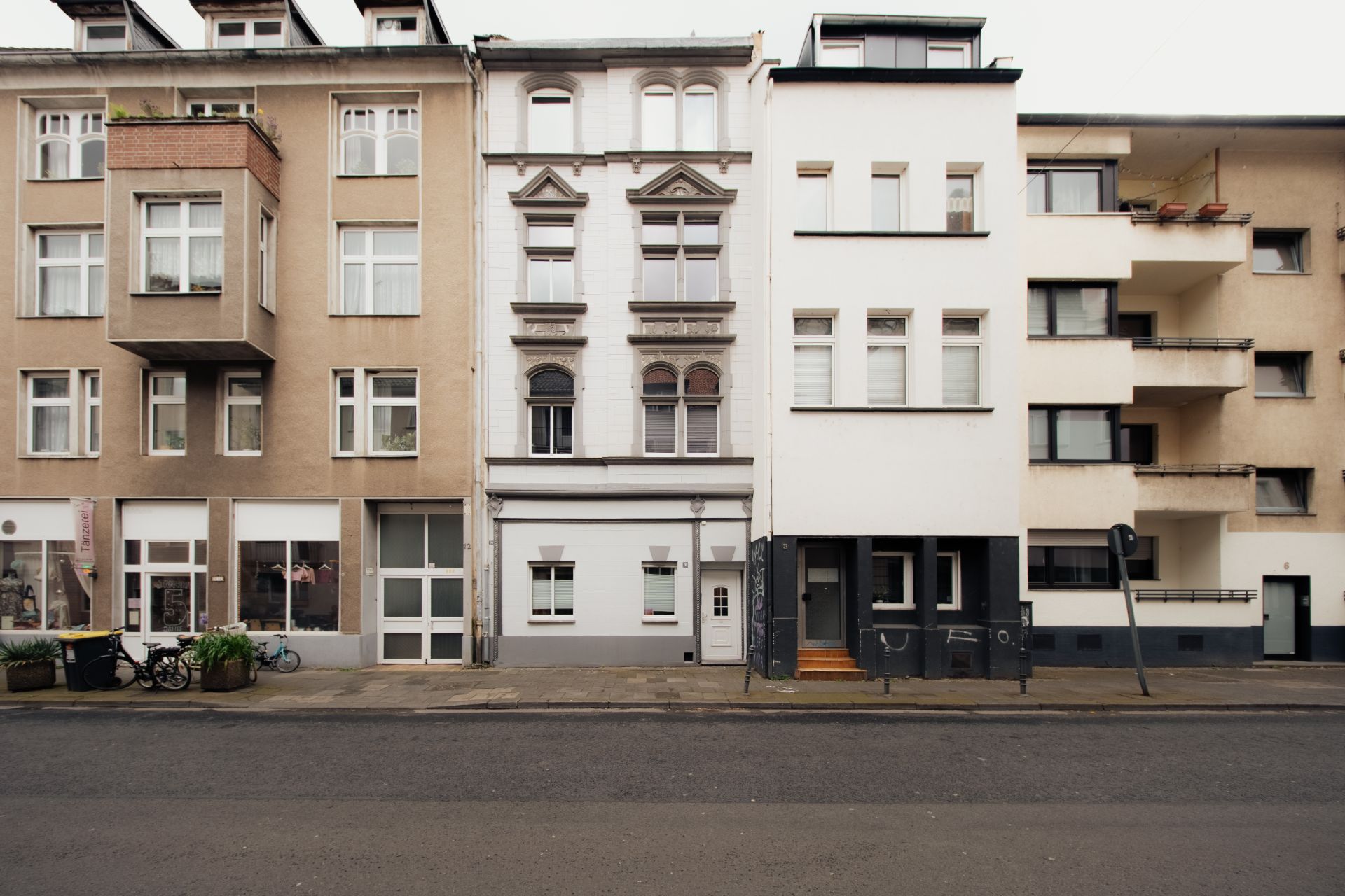 Mehrstöckige Wohnhäuser mit unterschiedlichen Fassaden stehen nebeneinander an einer ruhigen Straße.