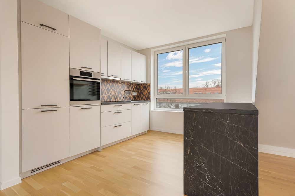 Moderne Küche mit weißen Schränken, Backofen, Holzboden und großem Fenster.
