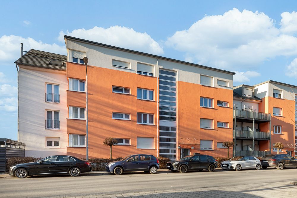 Mehrfamilienhaus mit orange-weißer Fassade, mehrere geparkte Autos davor.