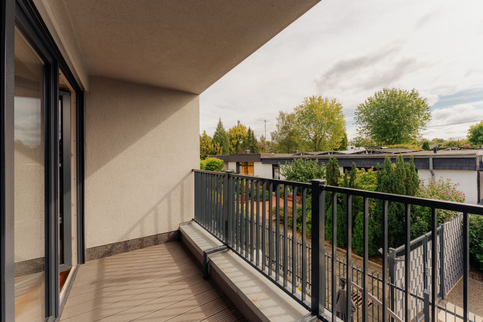 Balkon mit Metallgeländer, Blick auf Garten und benachbarte Häuser.