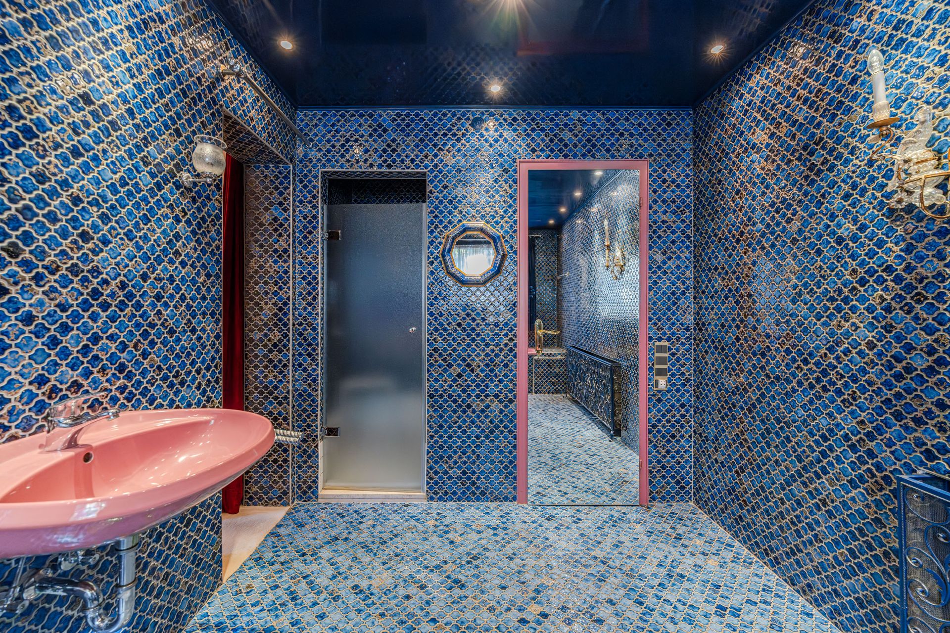 Badezimmer mit blauen Mosaikfliesen, rosa Waschbecken und Spiegel an der Wand.