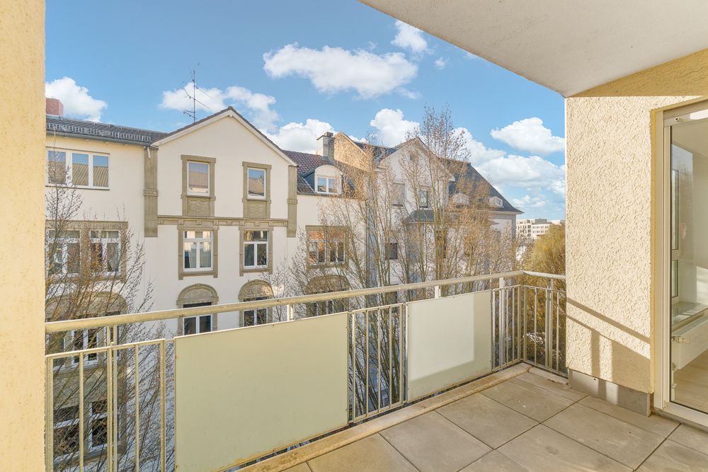 Balkon mit Geländer und Blick auf benachbarte Wohngebäude bei sonnigem Wetter.
