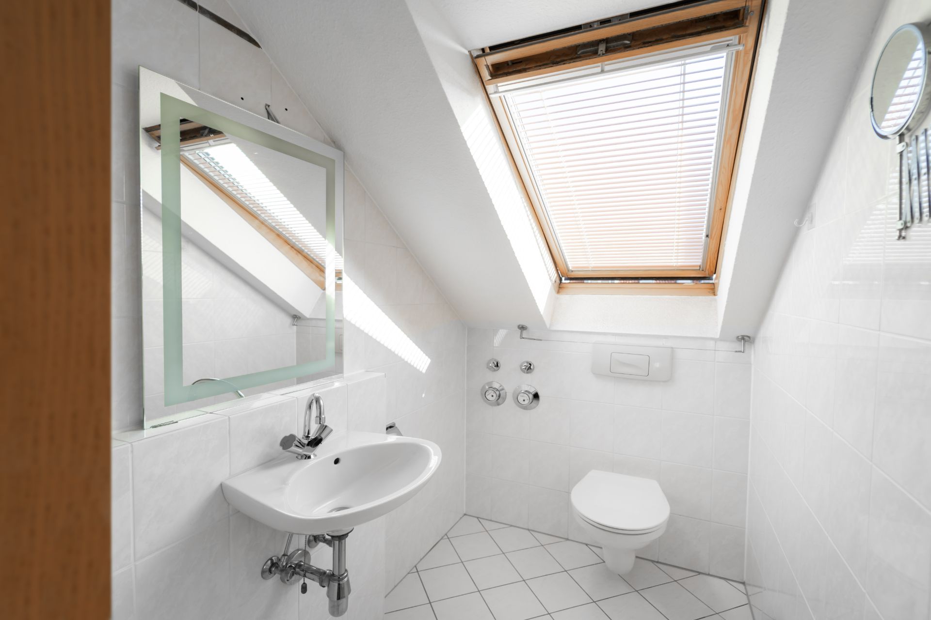 Helles Badezimmer mit Dachfenster, Waschbecken, Spiegel und Toilette.