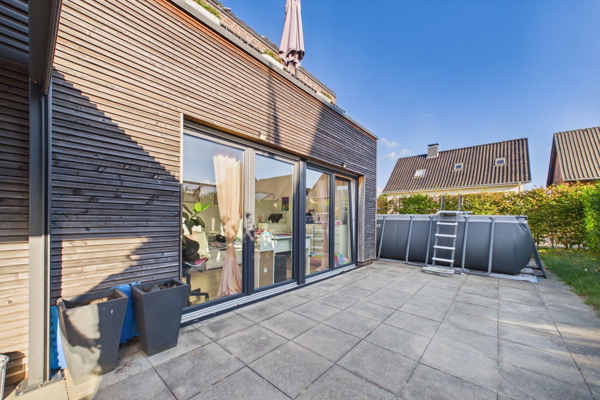 Moderne Terrasse mit Holzwand, großen Glastüren und aufgestelltem Pool im Garten.