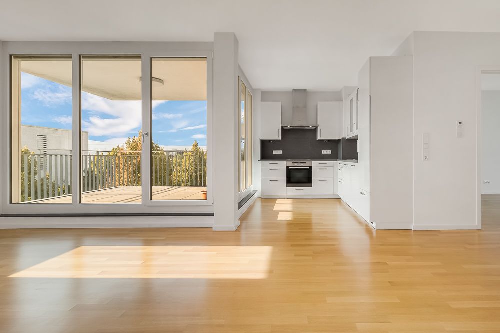 Heller Wohnraum mit offener Küche, großen Fenstern und Zugang zu einem Balkon.