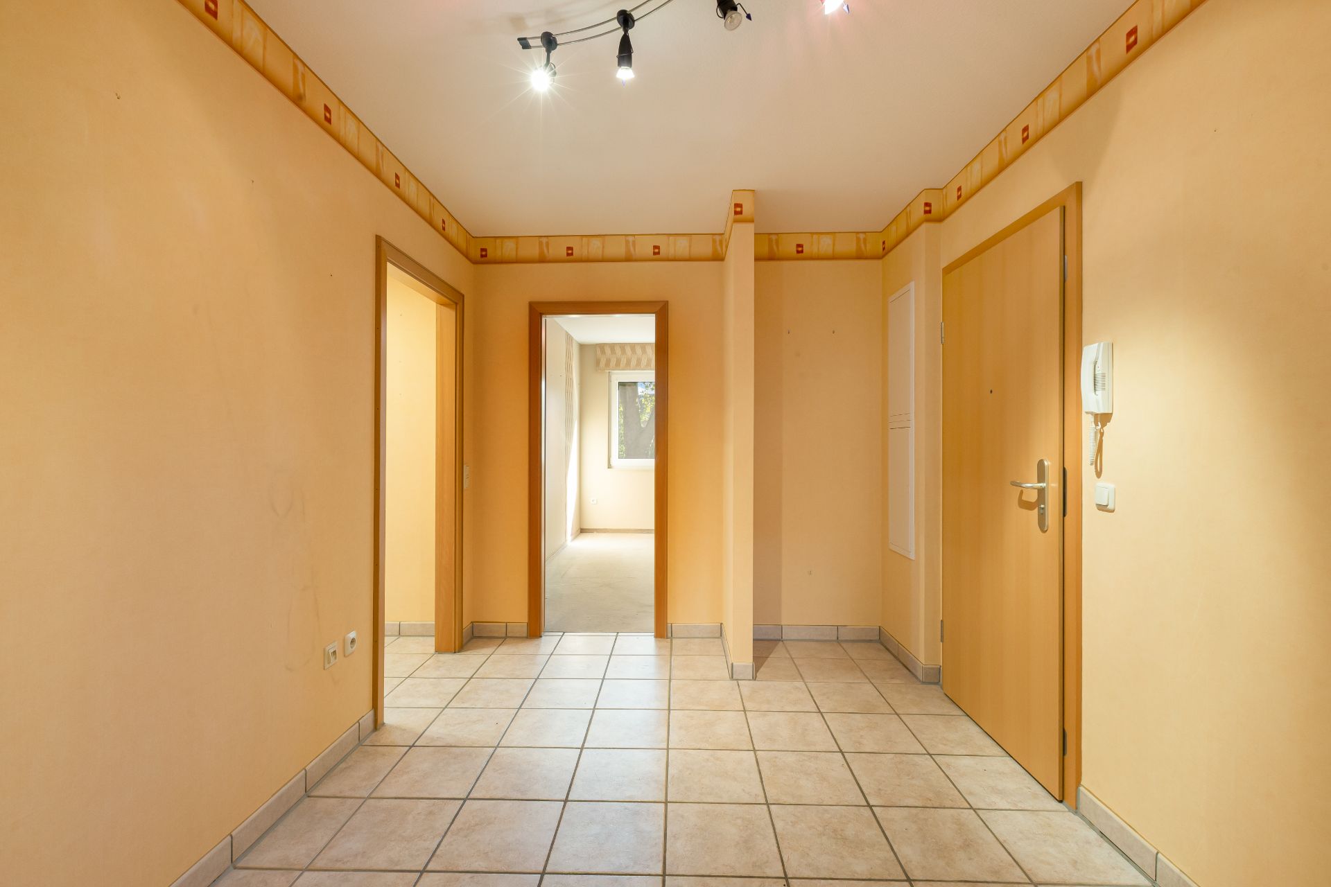 Heller Flur mit Fliesenboden, mehreren Türen und Deckenbeleuchtung in einer Wohnung.