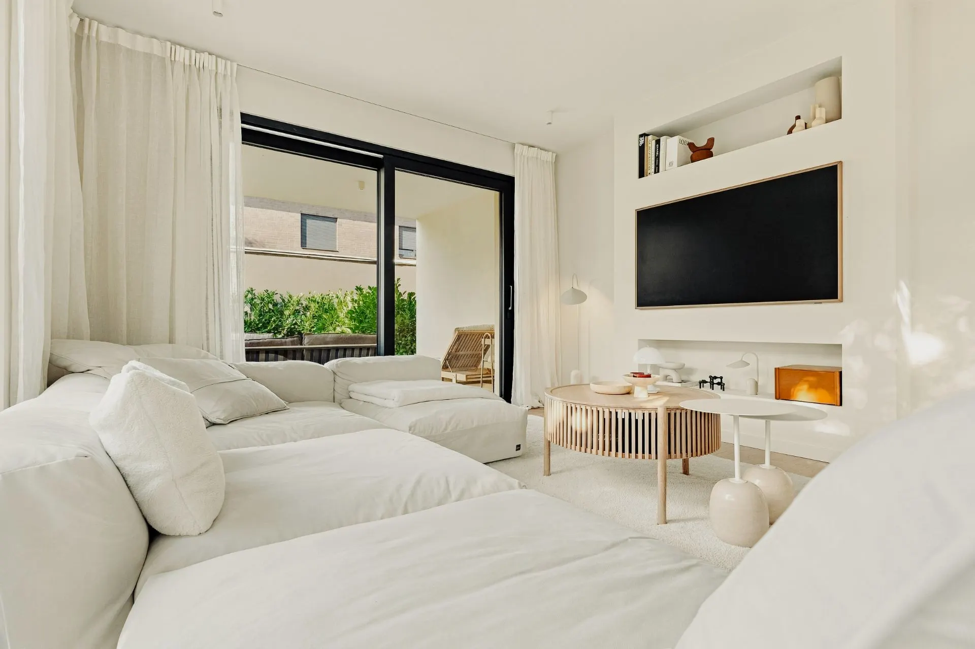 Helles Wohnzimmer mit weißem Sofa, Couchtisch, großem Fernseher und Zugang zu einer Terrasse.