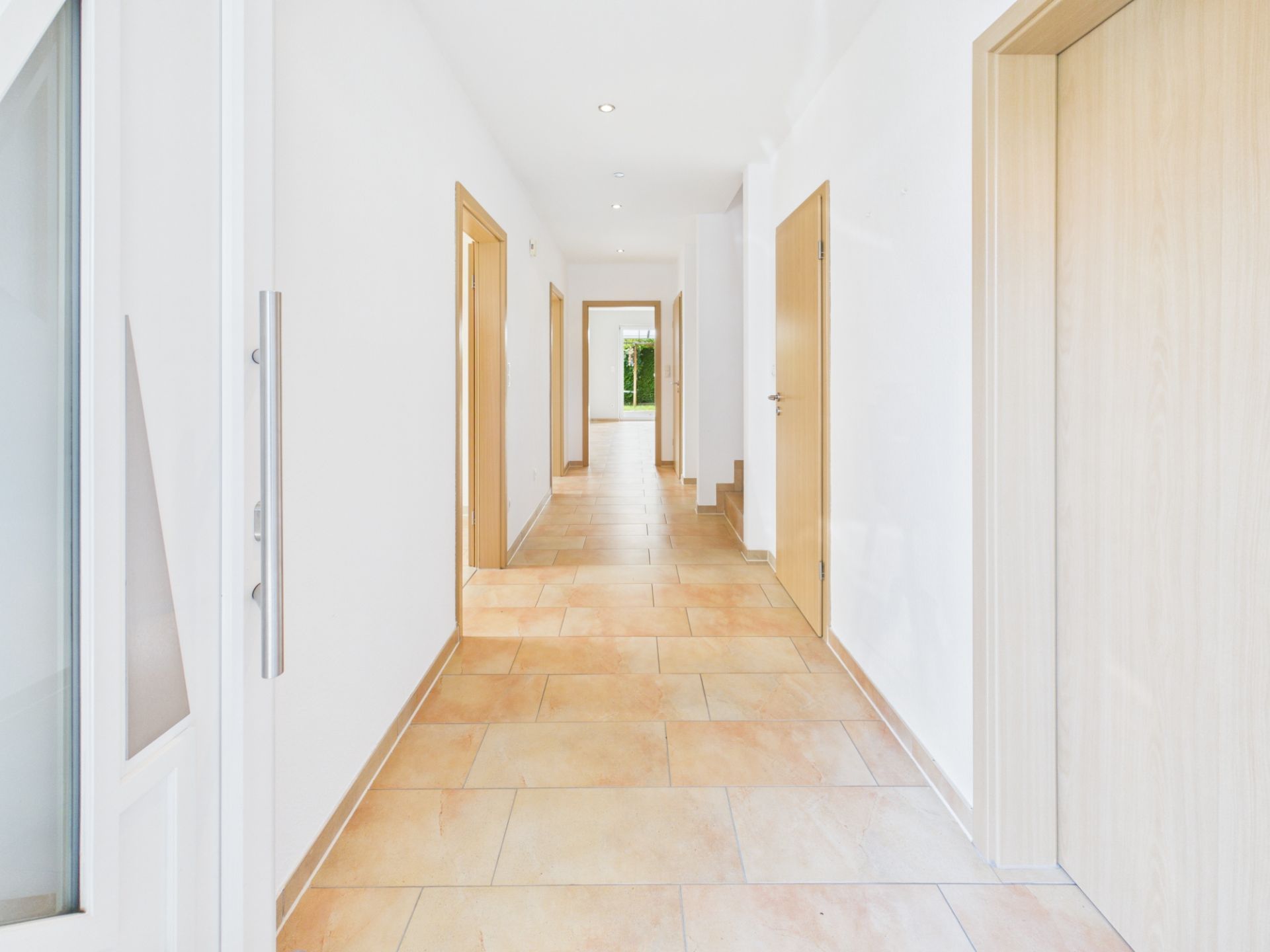 Heller Flur mit beigen Bodenfliesen und mehreren Holztüren in einem Wohnhaus.