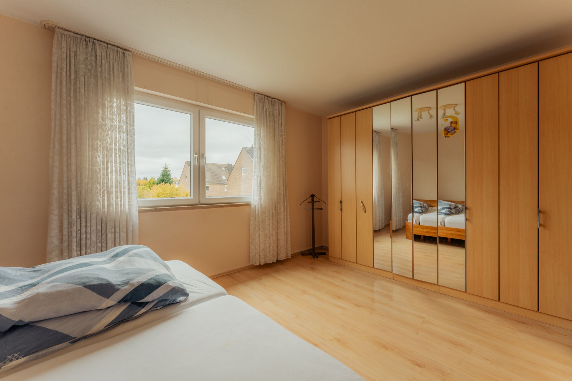 Schlafzimmer mit Doppelbett, großem Fenster und Spiegelschrank an der Wand.