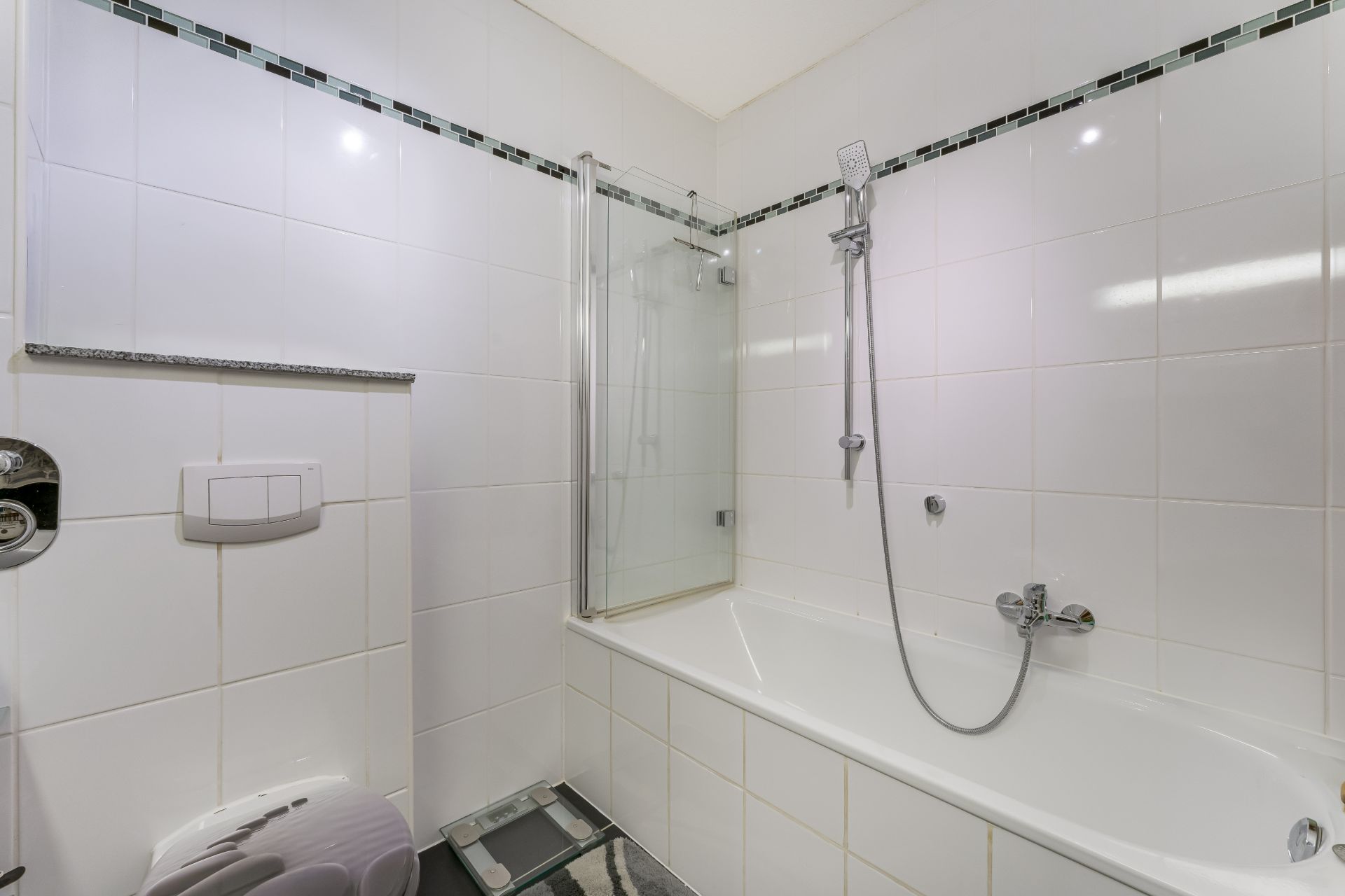 Modernes Bad mit weiß gefliester Wand, Badewanne, Glasdusche und Handbrause.