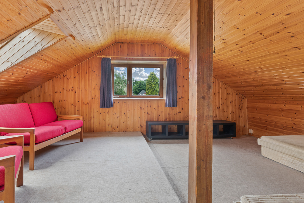 Wohnraum im Dachgeschoss mit Holzverkleidung, roten Sitzmöbeln und Fenster mit Ausblick.