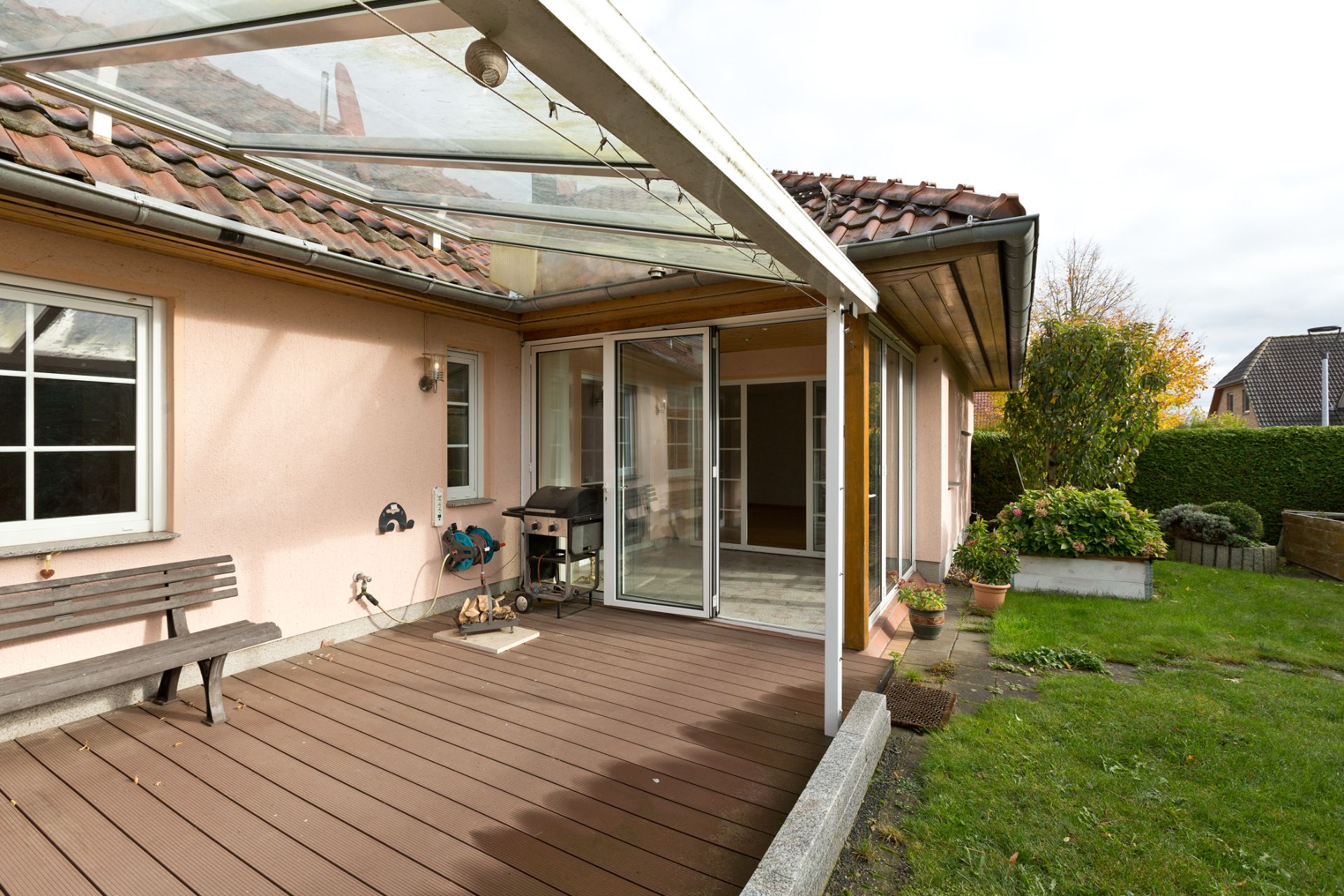 Überdachte Terrasse mit Sitzbank, Grill und Zugang zum Garten neben einem Haus.
