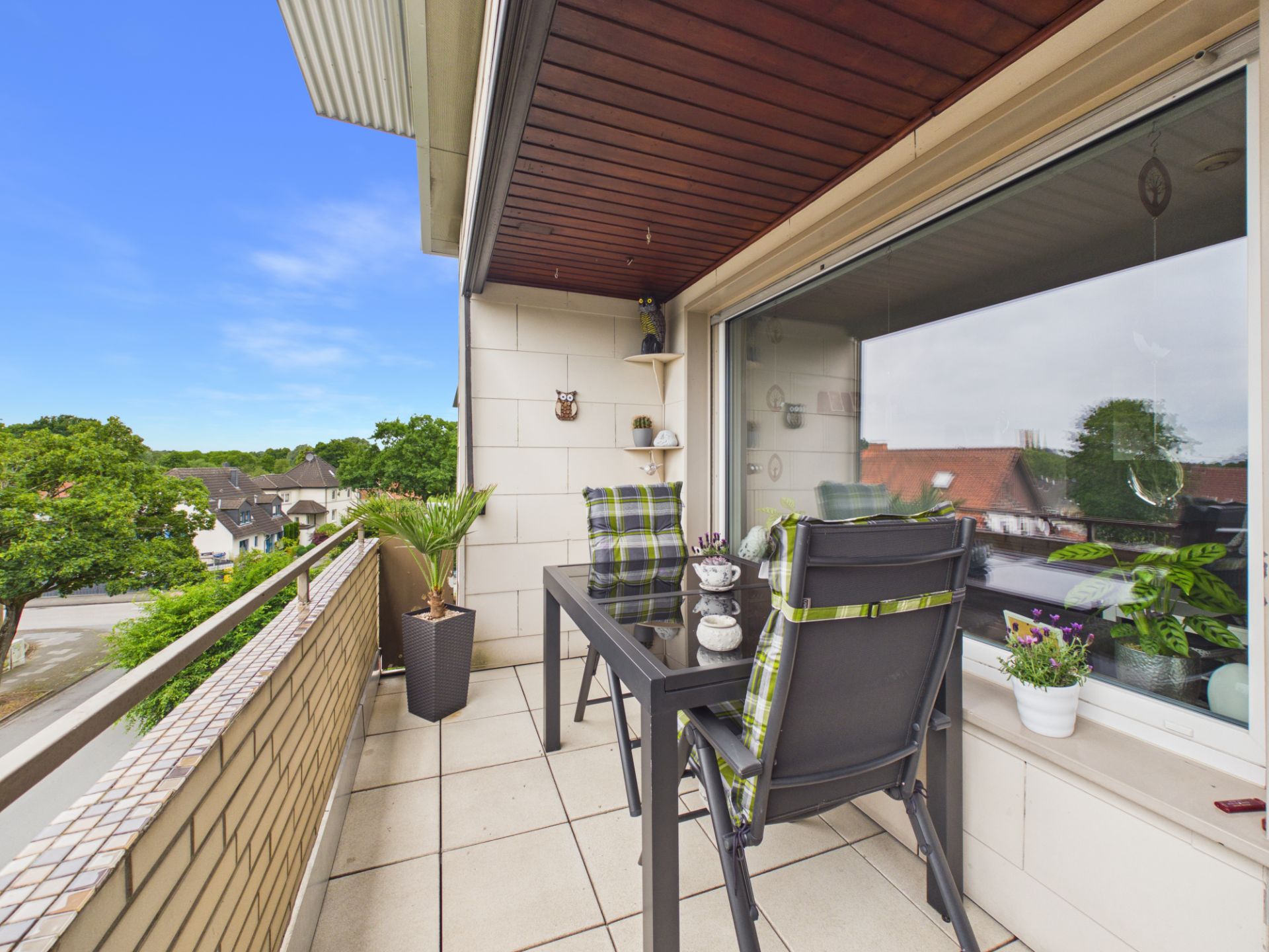 Balkon mit Tisch, zwei Stühlen, Pflanzen und Blick auf Bäume und Häuser.