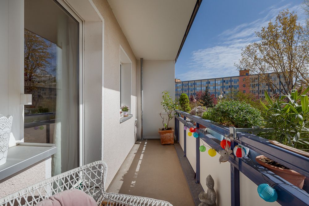 Balkon mit Pflanzen, bunten Lichterketten und Sitzmöbeln an einem sonnigen Tag.