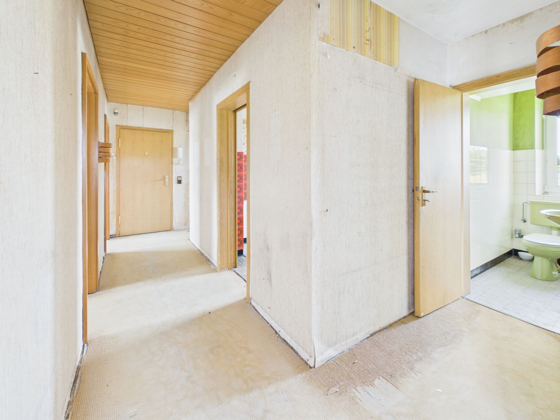 Heller Flur mit Holztüren, offener Tür zu einem Badezimmer mit grüner Keramik.