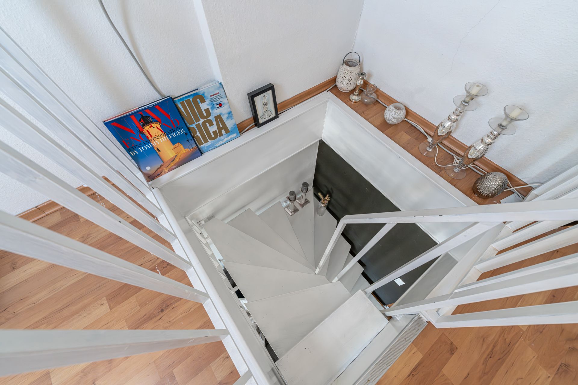 Weiße Treppe mit Holzgeländer. Bücher und Dekorationen stehen am Rand auf Holzfußboden.