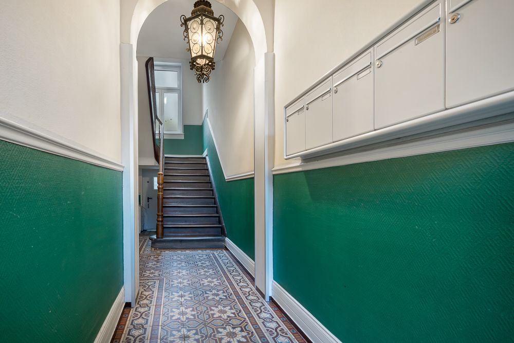 Hausflur mit grün gestrichenen Wänden, gemustertem Fliesenboden und Treppe.