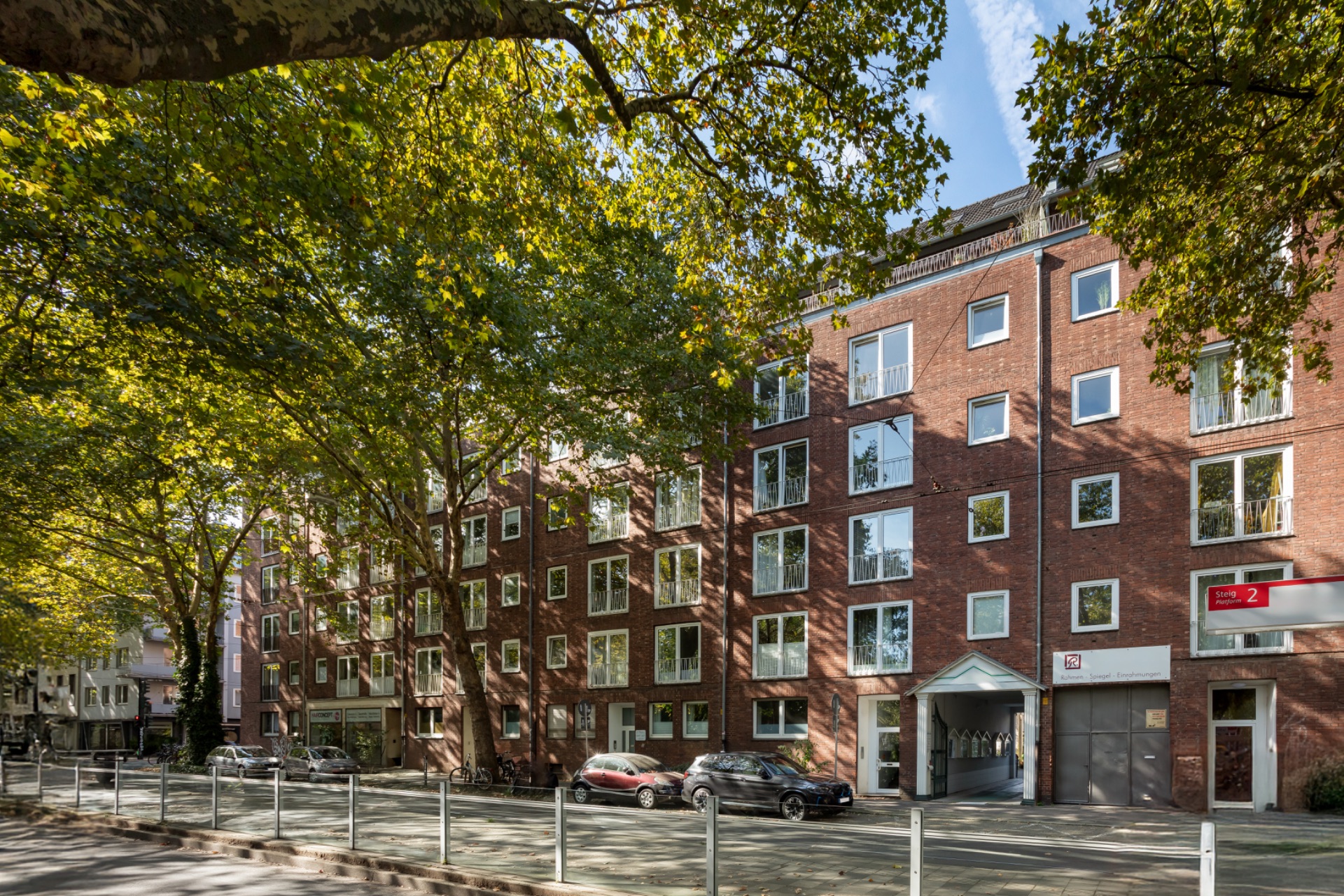 Mehrstöckiges Backsteingebäude mit vielen Fenstern und geparkten Autos vor dem Haus.