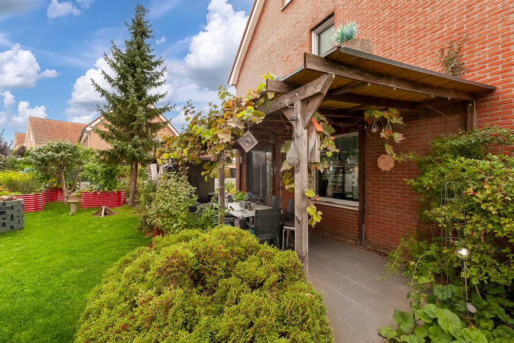 Gepflegter Garten mit überdachter Terrasse und Sitzbereich an einem roten Backsteinhaus.