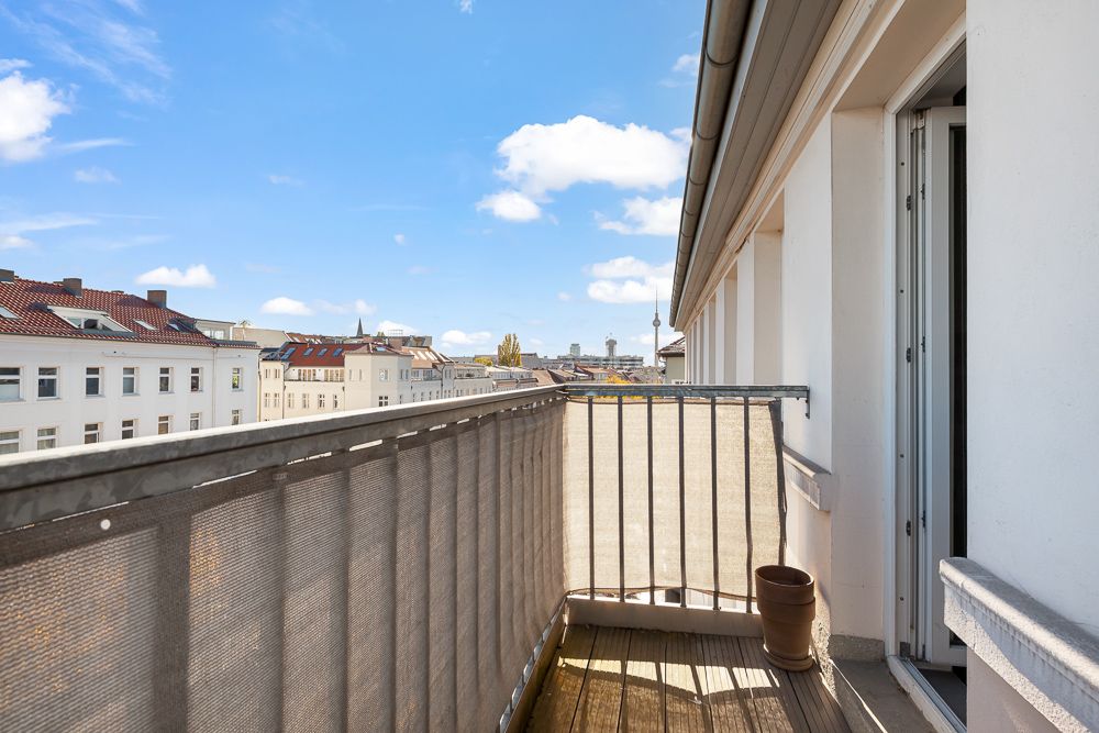Kleiner Balkon mit Holzboden und Topf, Blick auf umliegende Gebäude unter blauem Himmel.